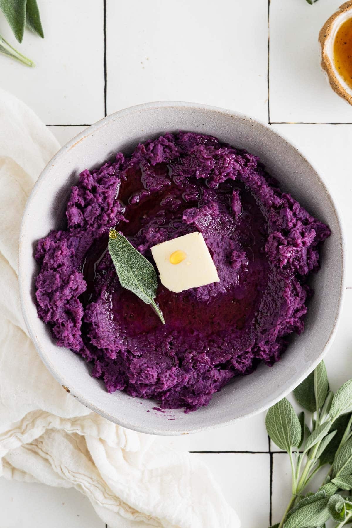 Vegan mashed sweet potatoes on white tile counter with fresh sage and butter.