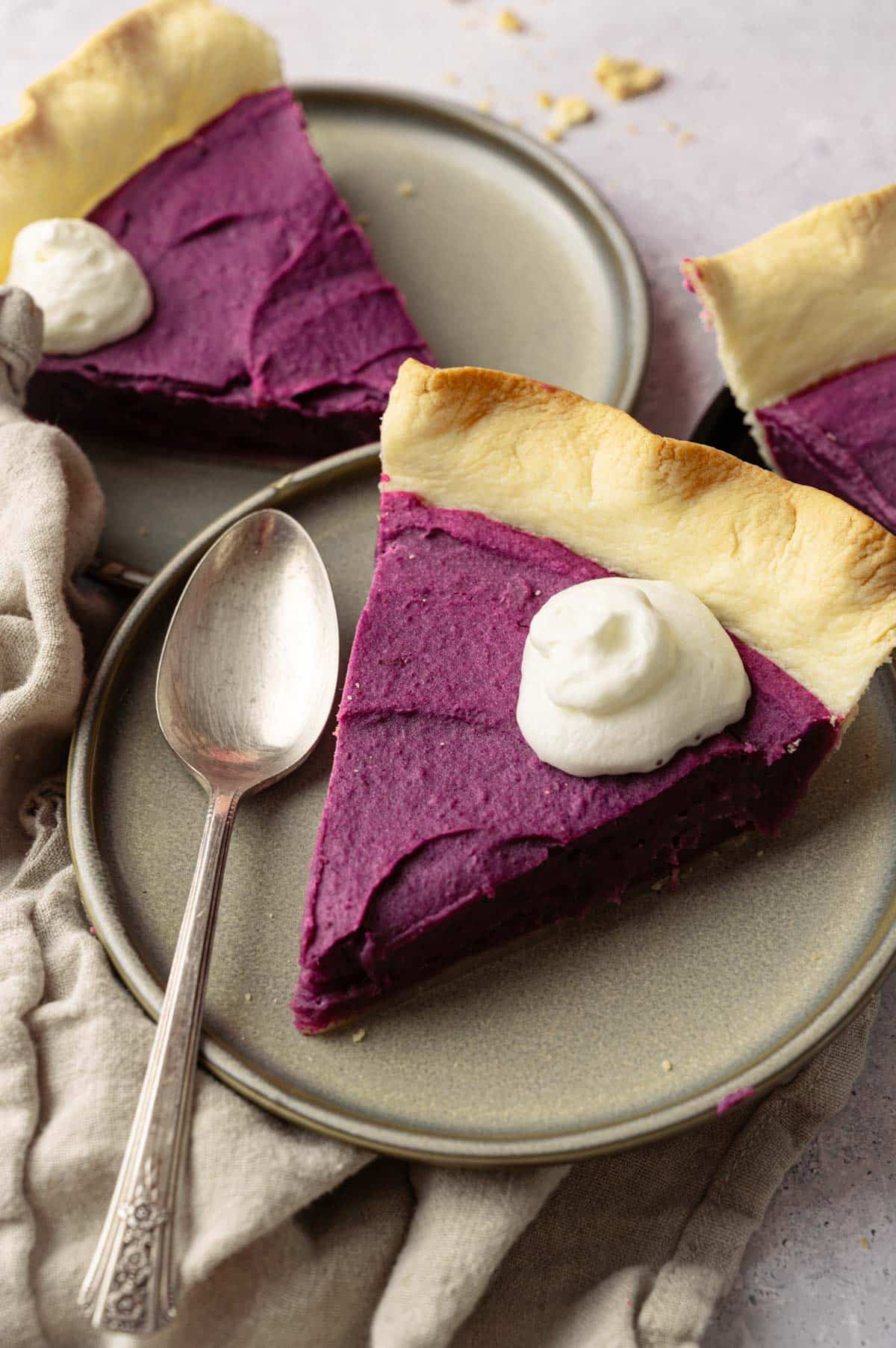 Close up of a slice of purple sweet potato pie with a spoon and whipped cream on top.