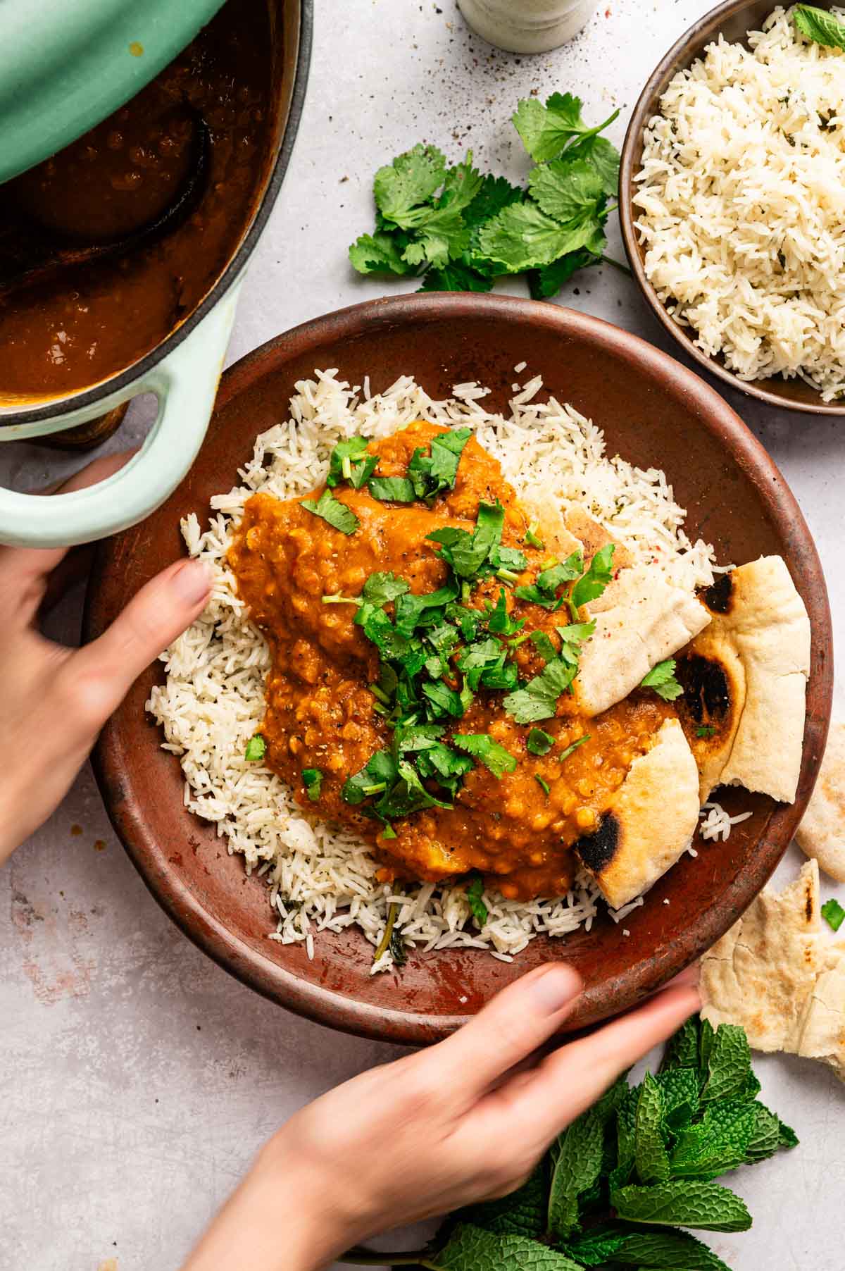 Woman reaching for plate of vegan potato tikka masala.