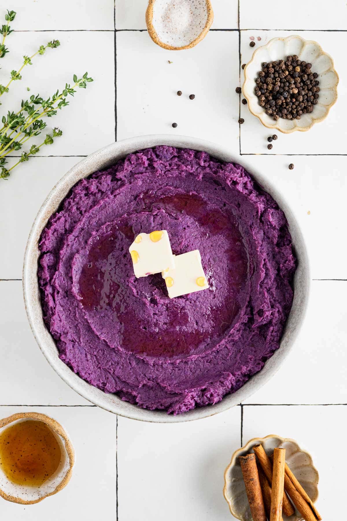 Whipped purple sweet potatoes in a grey shallow bowl with vegan butter, maple syrup, and thyme.
