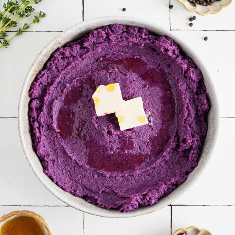 Whipped purple sweet potatoes in a grey shallow bowl with vegan butter, maple syrup, and thyme.