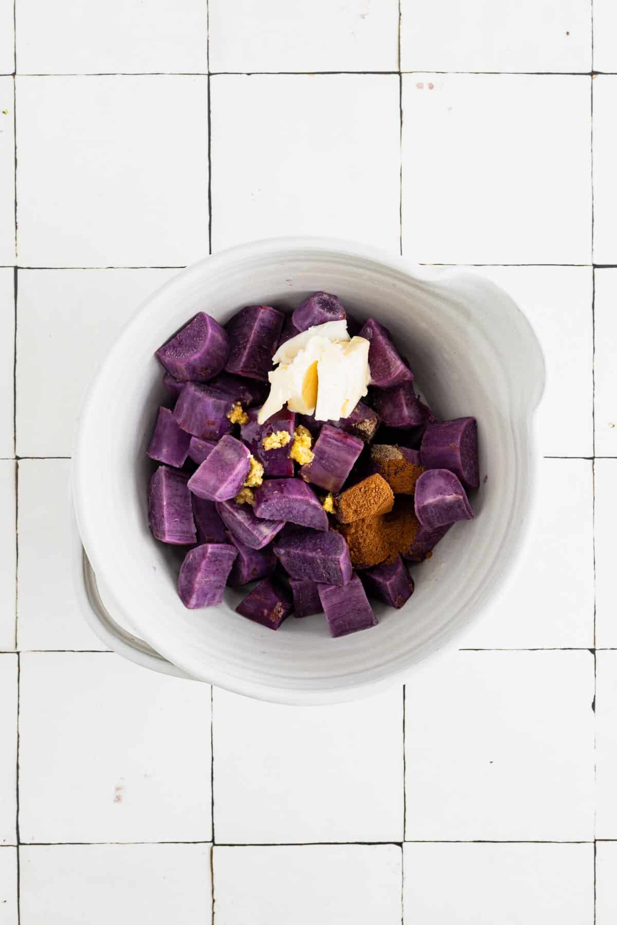 Cooked sweet potato chunks in a large white mixing bowl with spices.
