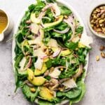 Arugula and spinach salad with sliced avocado, onion, pistachios, and shaved vegan Parmesan.