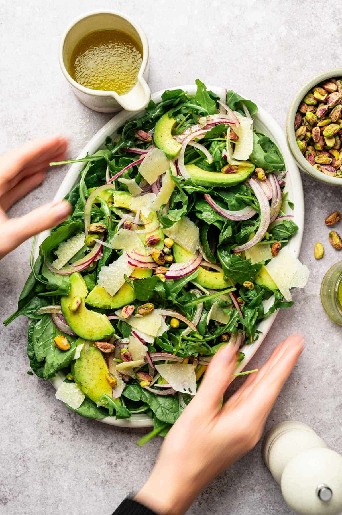 Woman reaching for a white platter filled with arugula spinach salad.