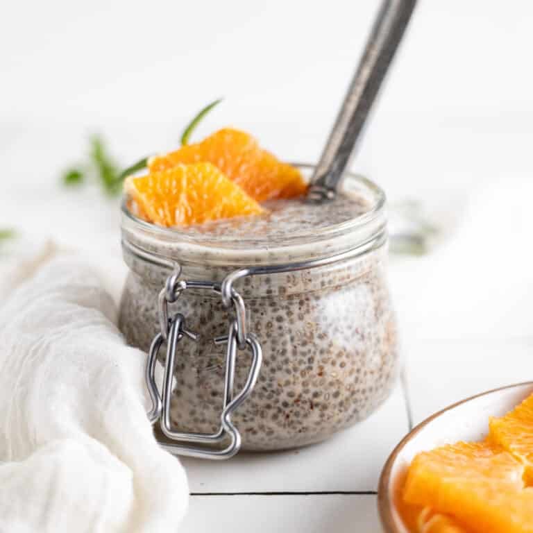 Homemade chia seed pudding with ground flax in a glass jar and orange slices and herbs on top.