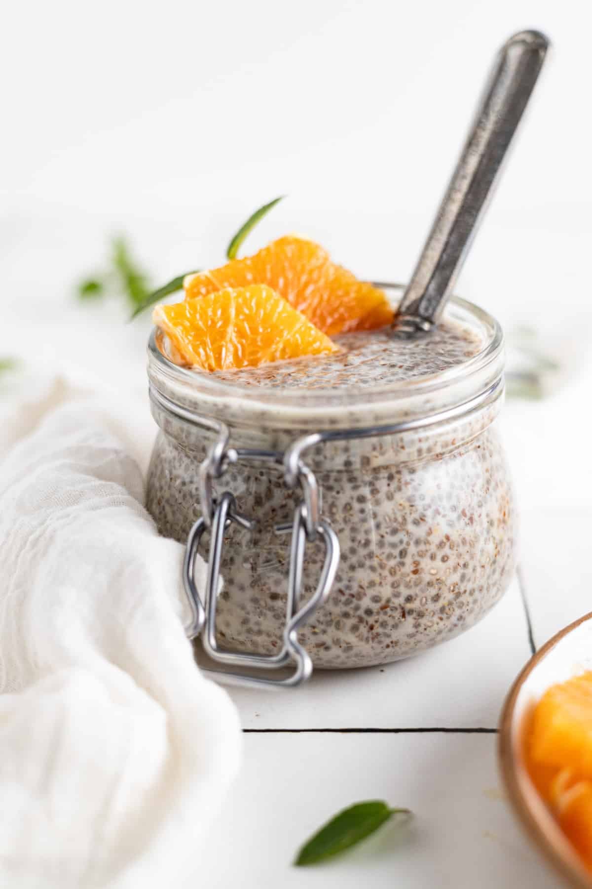Homemade chia seed pudding with ground flax in a glass jar and orange slices and herbs on top.