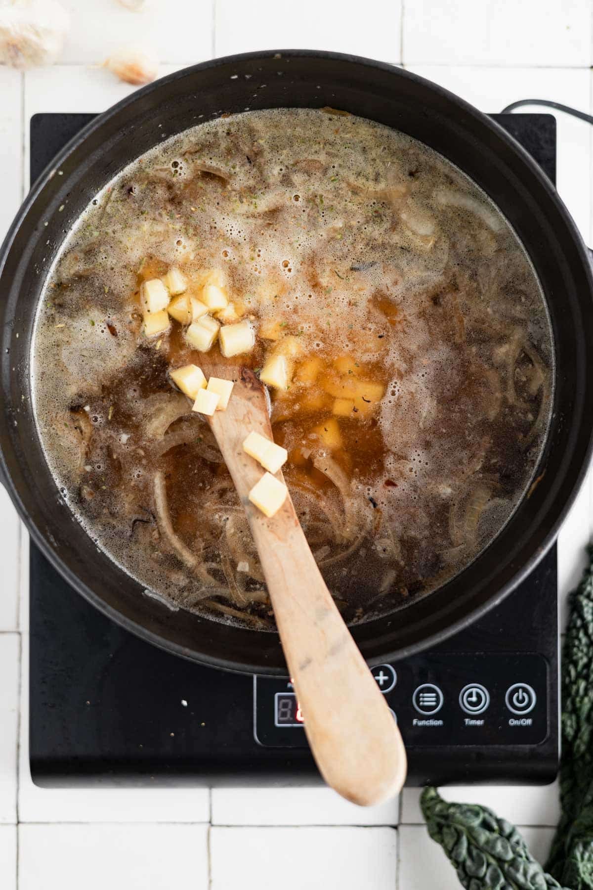 Wooden spoon stirring the ingredients in a medium black Dutch oven.
