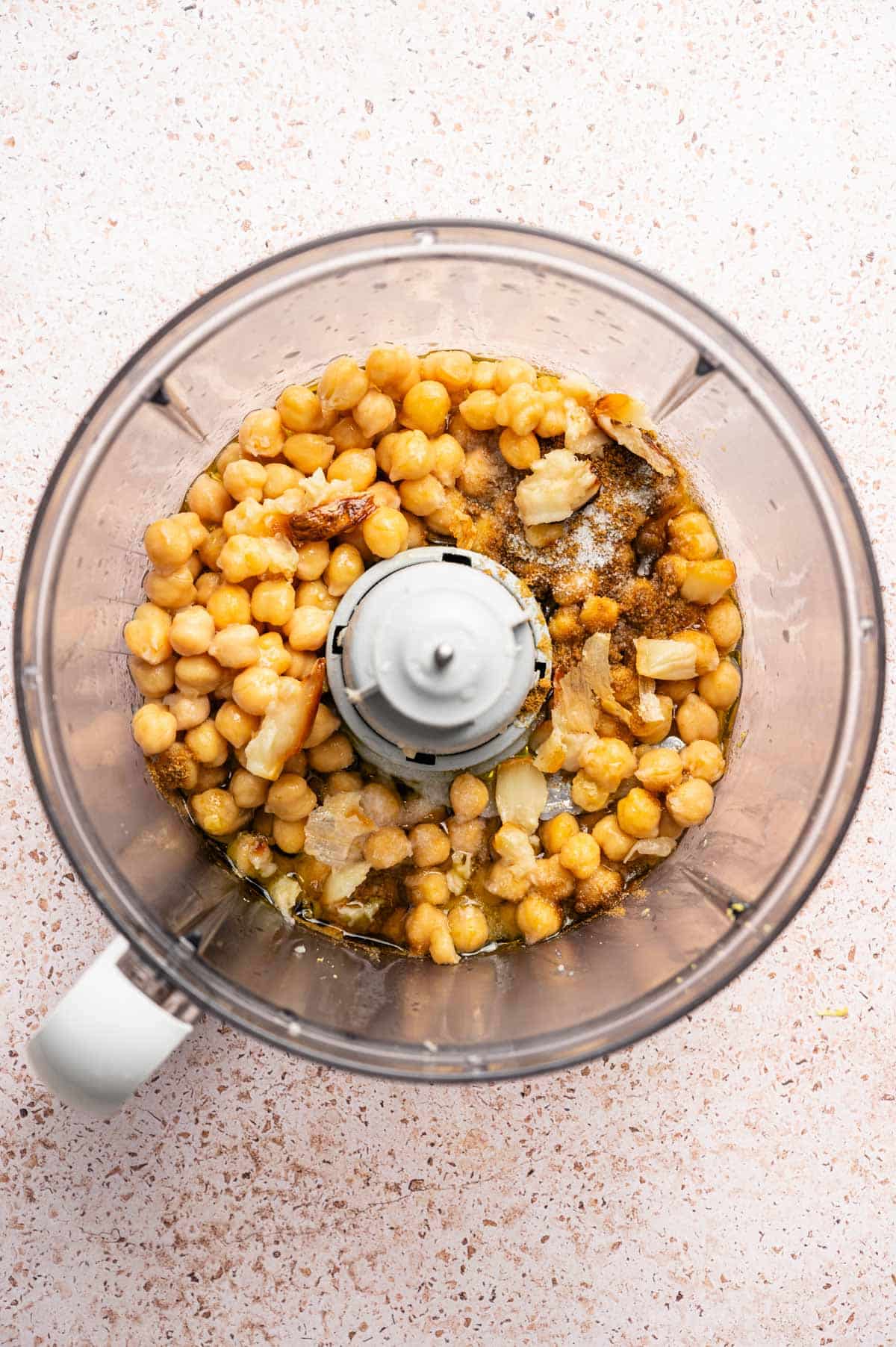 Chickpeas, garlic, and spices added to a food processor.