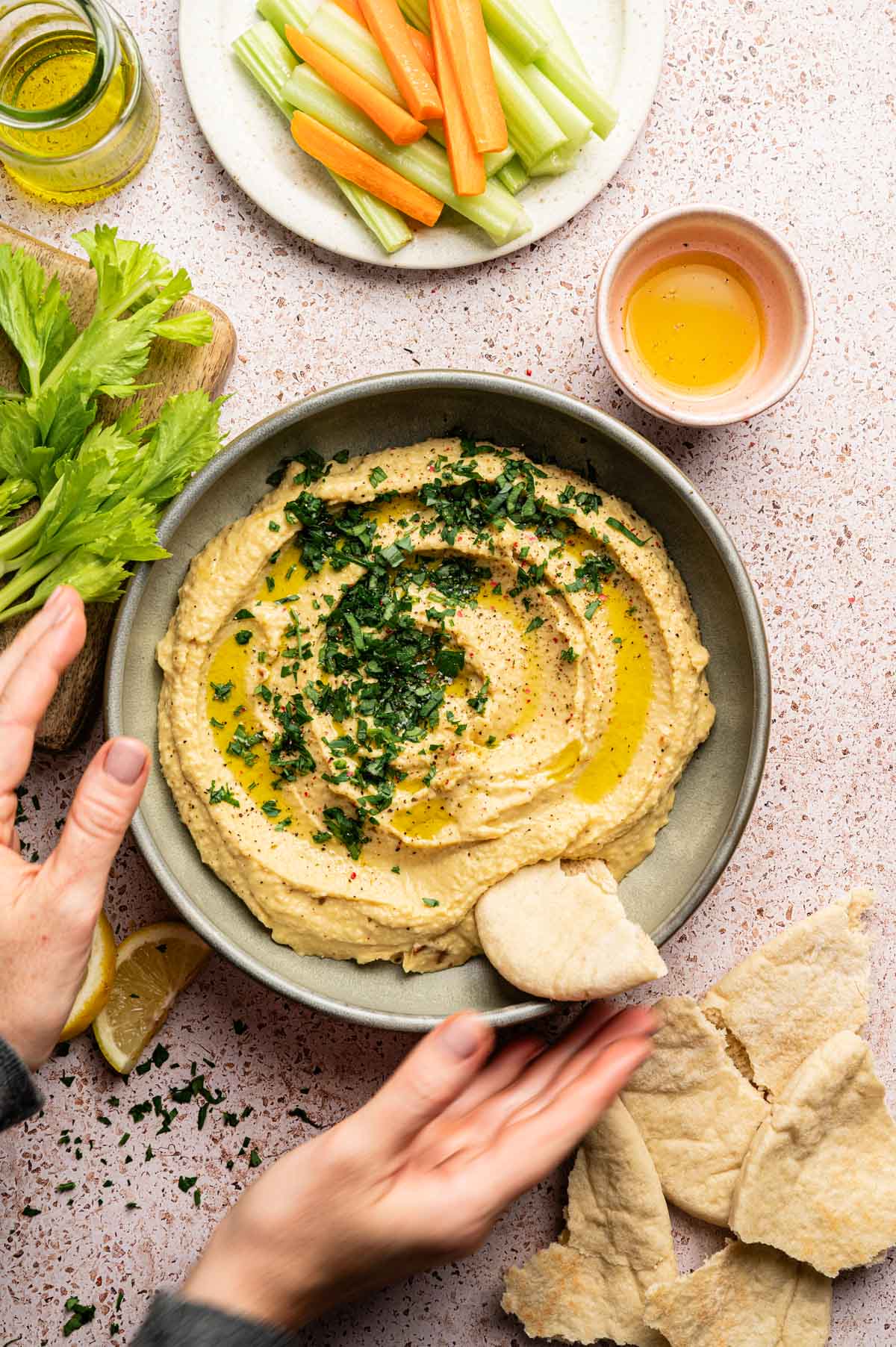 Roasted garlic hummus in a shallow green plate with olive oil and fresh herbs on top and pita bread.
