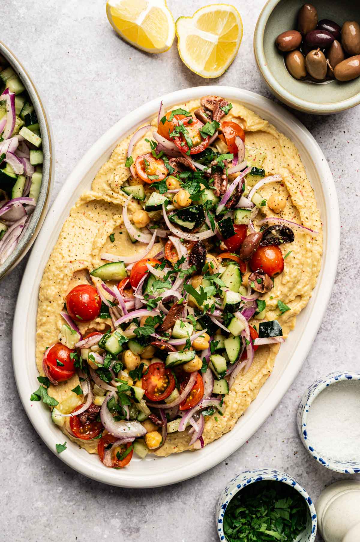 Freshly made hummus on a platter loaded with herby veggies.