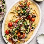 Freshly made hummus on a platter loaded with herby veggies.