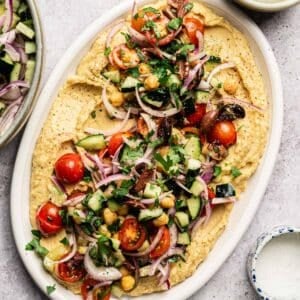 Freshly made hummus on a platter loaded with herby veggies.