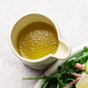 Dijon maple vinaigrette in a white carafe next to a salad.