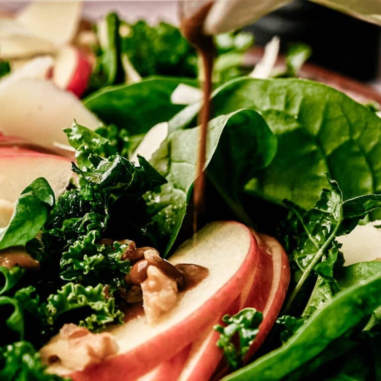 Balsamic basil salad dressing being drizzled on top of a kale and spinach salad.