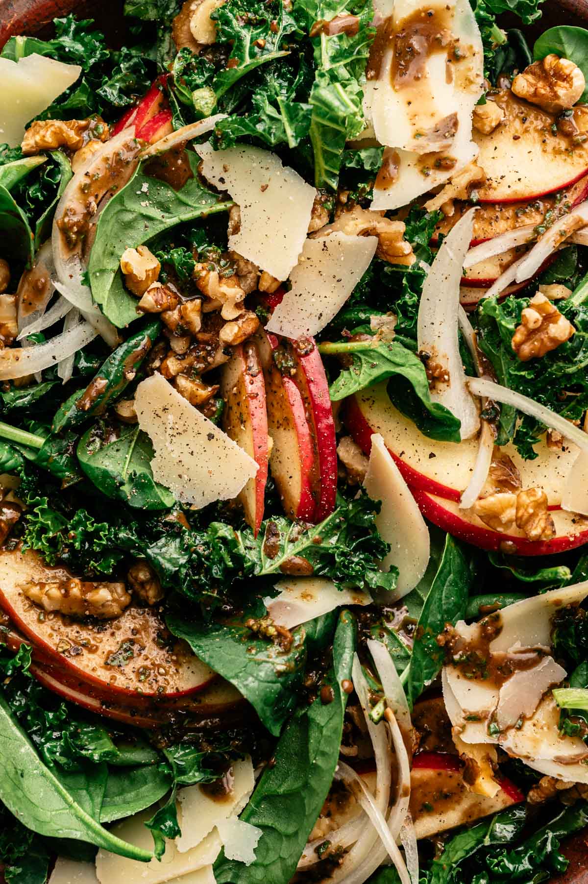 Close up of spinach kale salad recipe with sliced onion, apples, walnuts, vegan parmesan, and homemade basil balsamic dressing.