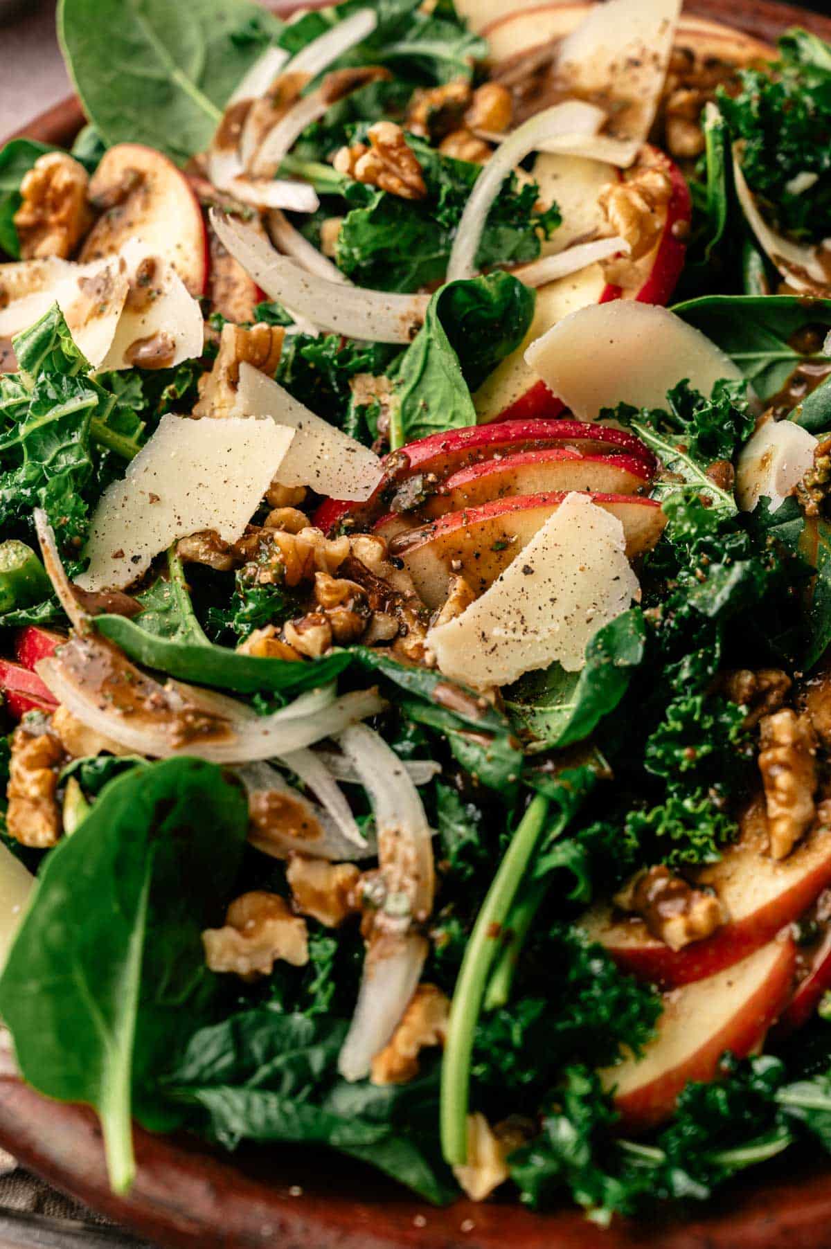 Close up of spinach kale salad recipe with sliced onion, apples, walnuts, vegan parmesan, and homemade basil balsamic dressing.