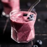 Close up of pink smoothie in clear glass cups with a glass straw sticking out.