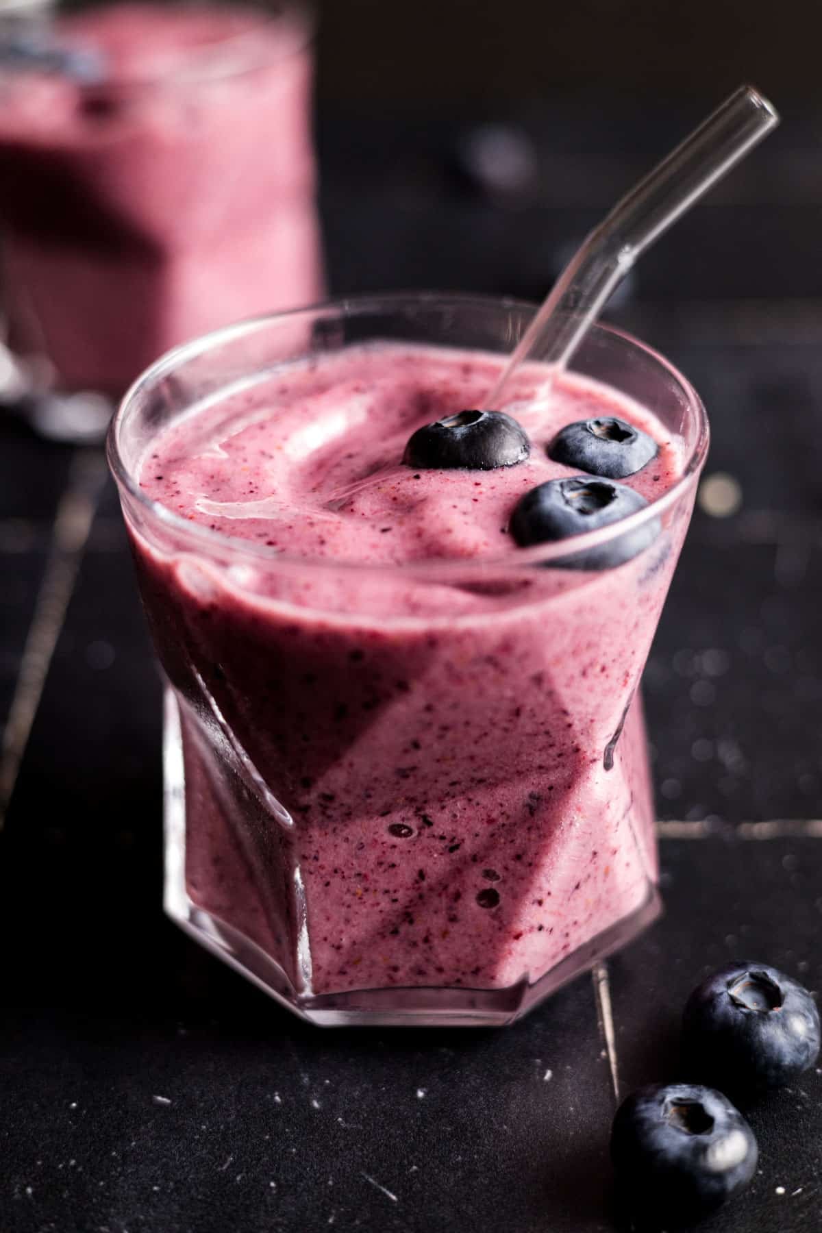 Close up of pink smoothie in clear glass cups with a glass straw sticking out.